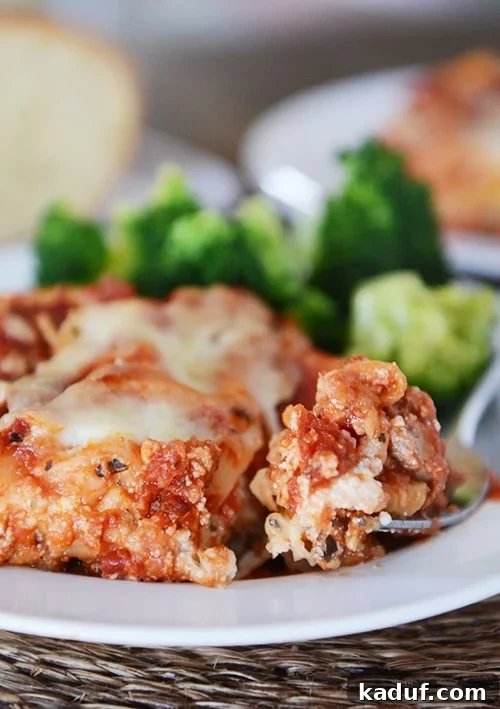 Mom's Signature Lasagna 2 Broccoli and a piece of lasagna with a bite being taken out with a fork on a white plate. A perfect slice of classic lasagna ready to be enjoyed.