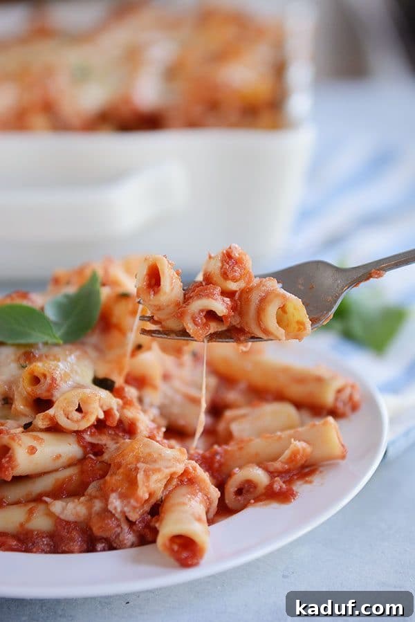 Hearty Make-Ahead Cheesy Baked Ziti 3 A fork taking a bite of cheesy red sauce baked ziti off of a white plate.