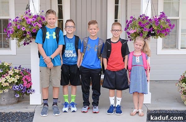 Five excited children stand on their front porch on their first day of school, backpacks ready.