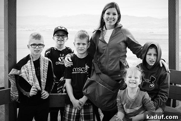 A loving mother stands with her five children in front of a bright window, showcasing family connection.