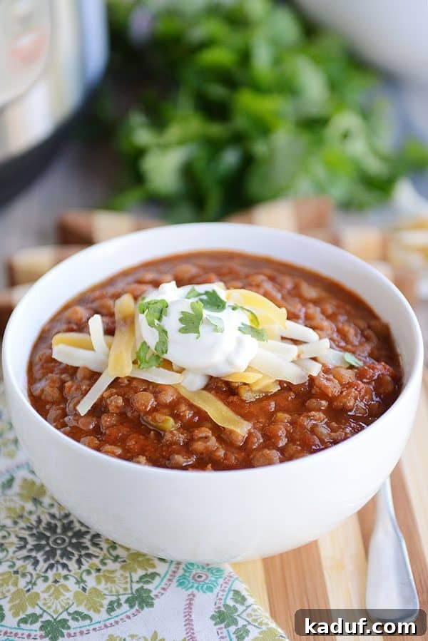 A white bowl of hearty lentil chili generously topped with sour cream and shredded cheddar cheese.