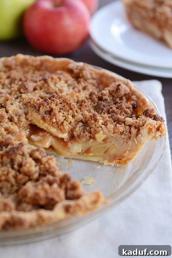 Simple Apple Crumble Pie 3 A beautifully baked apple crumble pie cooling in a clear glass pie dish, with a single slice already removed, revealing its delicious filling.