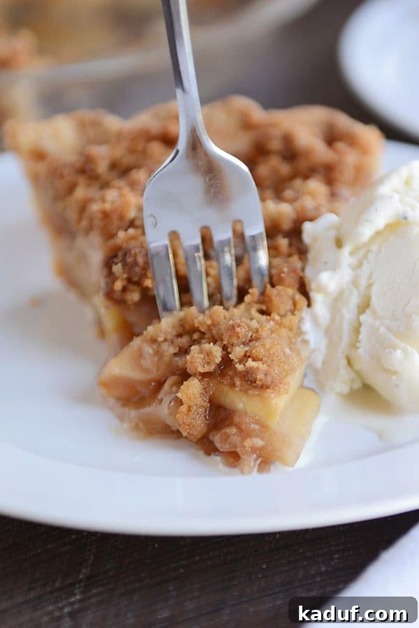 Simple Apple Crumble Pie 4 A fork lifts a mouth-watering bite of apple crumble pie from a slice, showcasing the tender apples and crisp topping.