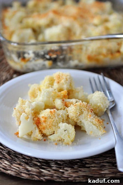 Golden Cheesy Cauliflower Gratin 2 A white plate featuring a generous serving of perfectly baked cheesy cauliflower, with a fork resting beside it, ready to be enjoyed.