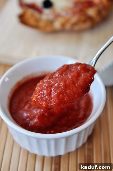 Effortless Homemade No-Cook Pizza Sauce 9 A spoonful of rich, homemade pizza sauce being lifted out of a small ramekin, ready to taste.