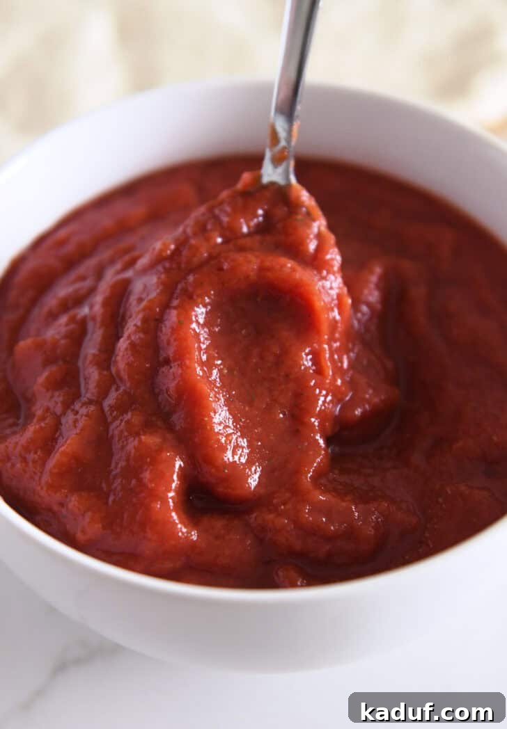 Effortless Homemade No-Cook Pizza Sauce 5 A metal spoon stirring a bowl of vibrant, homemade no-cook pizza sauce, showcasing its perfect consistency.