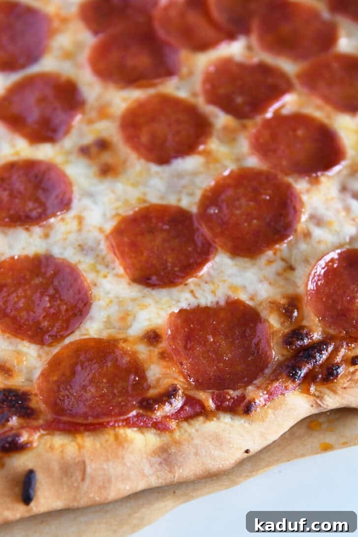 Effortless Homemade No-Cook Pizza Sauce 7 A freshly baked pepperoni pizza with a golden crust on parchment paper, ready to be sliced.
