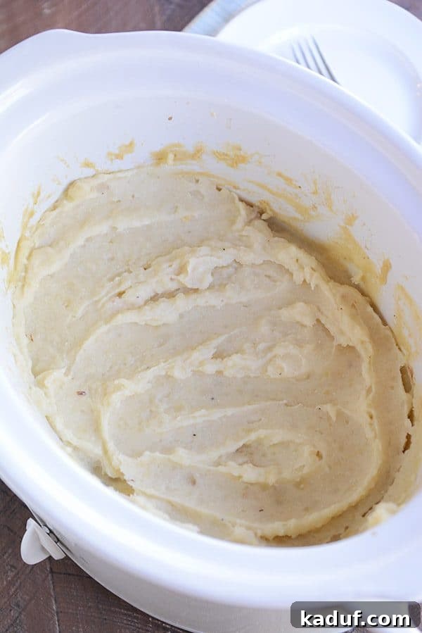 Effortless Slow Cooker Creamy Mash 2 A white crockpot full of creamy mashed potatoes, ready to be served or mashed.