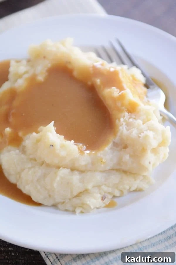 Effortless Slow Cooker Creamy Mash 3 A white plate with a large serving of mashed potatoes covered in rich brown gravy, highlighting the creamy texture.