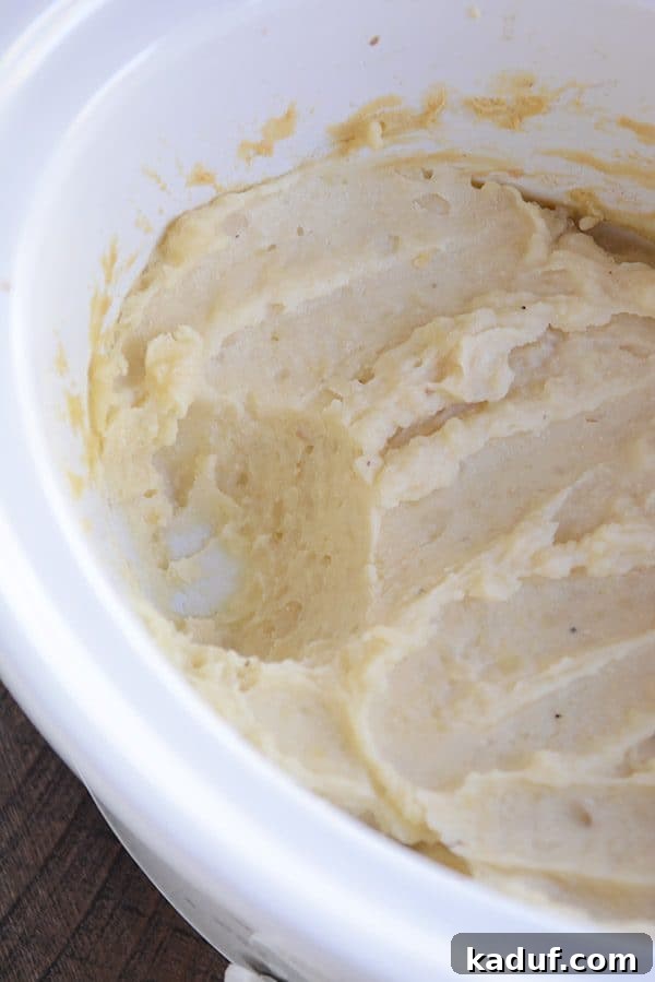 Effortless Slow Cooker Creamy Mash 4 A white crockpot full of unmashed cooked potatoes, showing the tender consistency before final mashing.