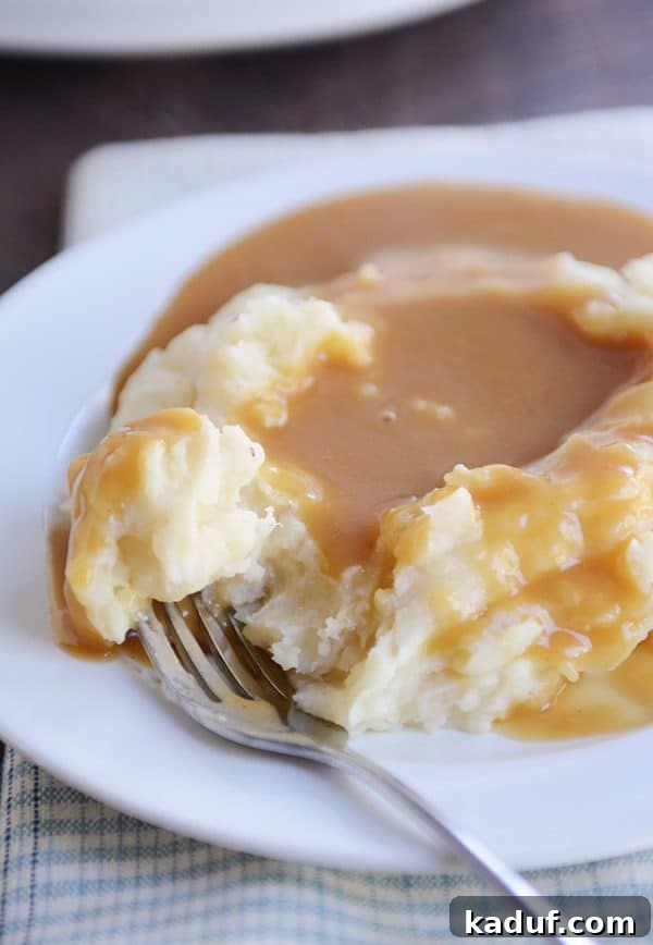 Effortless Slow Cooker Creamy Mash 5 Mashed potatoes covered in brown gravy on a white plate, ready to be eaten.
