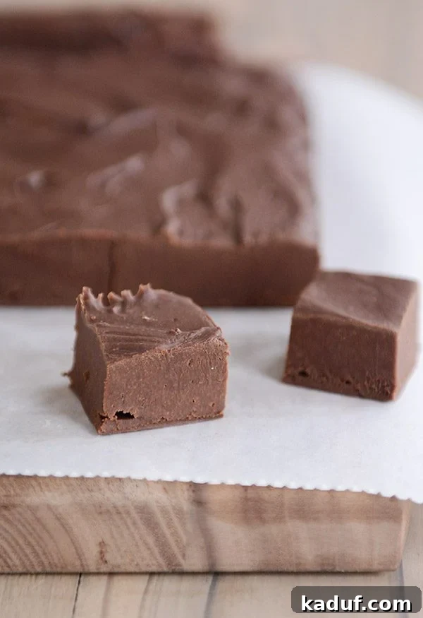 Foolproof Fudge Infinite Flavor Possibilities 2 A pristine brick of chocolate fudge with two perfectly cut squares placed invitingly in front, all resting on elegant parchment paper. This visually rich image emphasizes the fudge's tempting texture and homemade quality.
