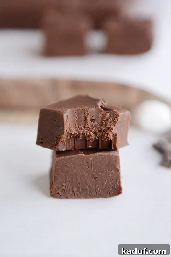 Foolproof Fudge Infinite Flavor Possibilities 6 Two squares of decadent homemade fudge are stacked, with a tempting bite taken out of the top piece. More fudge squares are softly blurred in the background, inviting you to indulge in this easy-to-make, creamy chocolate treat.