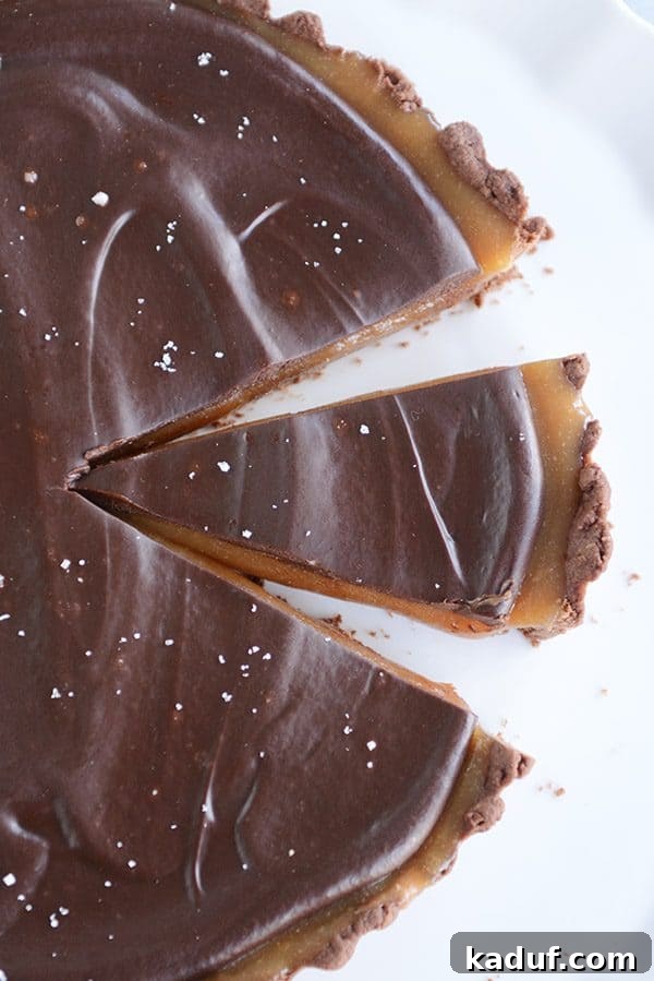 Rich Chocolate Caramel Tart 2 Top view of a chocolate caramel tart with a slice cut out, showcasing the distinct layers of chocolate crust, golden caramel, and glossy ganache.
