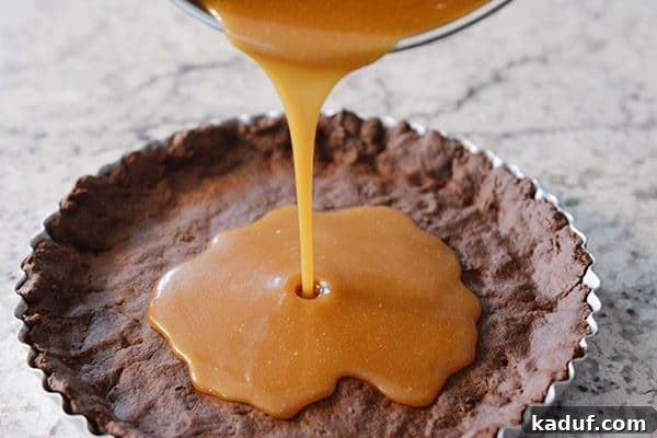 Rich Chocolate Caramel Tart 4 Smooth, golden caramel being carefully poured into a baked chocolate tart crust.