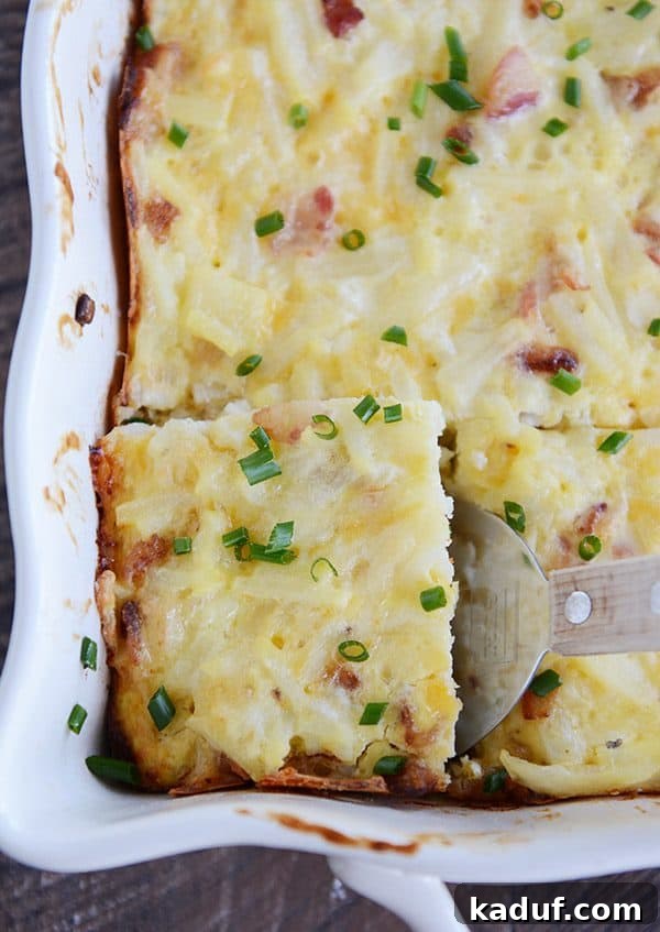Rich Cheesy Hash Brown and Egg Overnight Bake 2 A dish full of cheesy egg casserole sprinkled with green onion. The front left piece is cut and being scooped out.