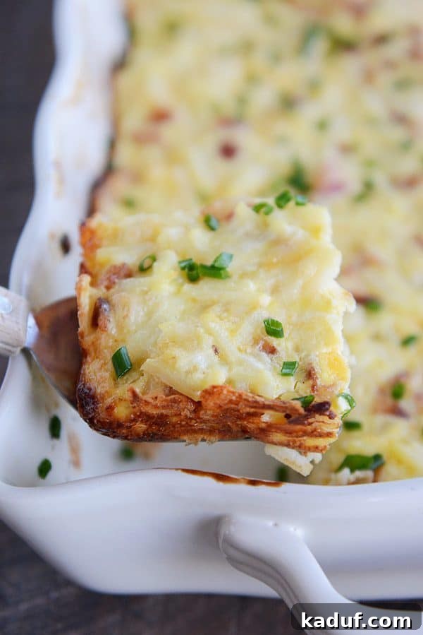 Rich Cheesy Hash Brown and Egg Overnight Bake 6 A dish full of cheesy egg casserole sprinkled with green onion. The front left piece is cut and being scooped out.