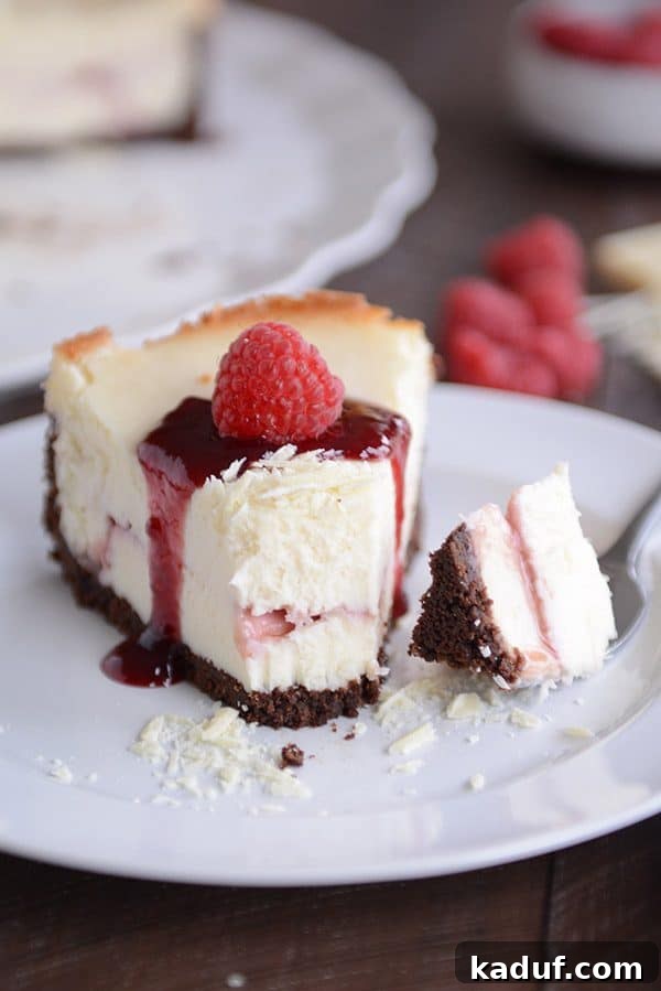 Exquisite White Chocolate Raspberry Truffle Cheesecake 5 A close-up shot of a fork lifting a piece of the White Chocolate Raspberry Truffle Cheesecake, emphasizing its rich, creamy texture and the perfect integration of the raspberry swirl.
