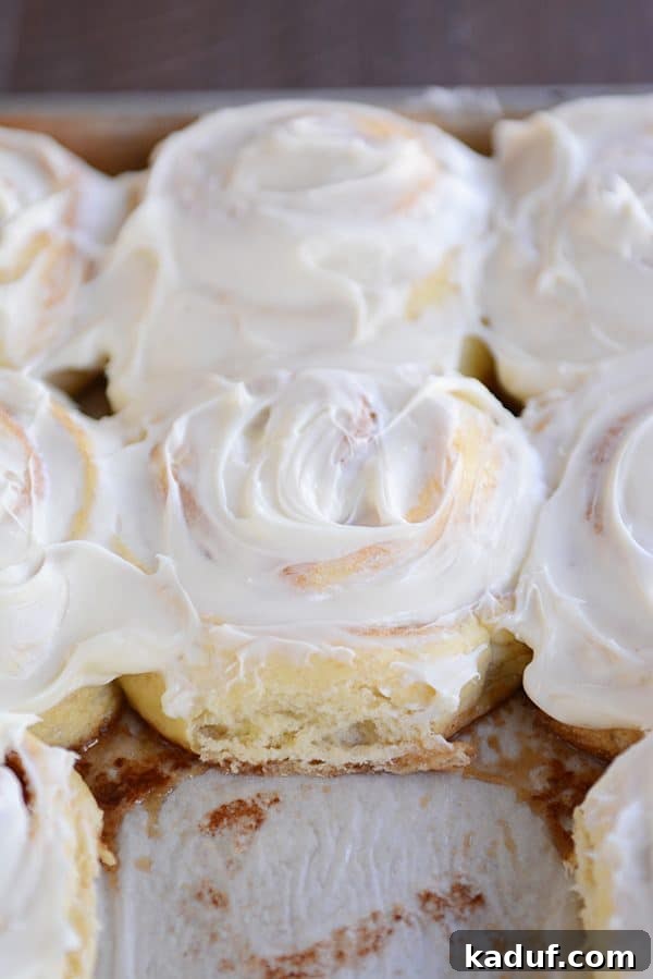 Overnight Cinnamon Rolls for Effortless Mornings 2 A baking pan filled with frosted cinnamon rolls, with one roll enticingly pulled out, ready to be enjoyed.
