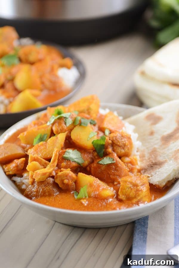 Creamy Instant Pot Indian Butter Chicken with Tender Potatoes 2 A bowl of white rice topped with Instant Pot Indian butter chicken and potato curry, garnished with fresh cilantro.