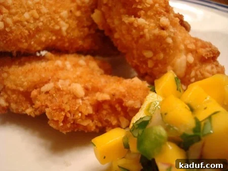 Tropical Macadamia Chicken with Sweet Mango Salsa 2 Crispy macadamia-crusted chicken with vibrant mango salsa on a pristine white plate, garnished with fresh cilantro.