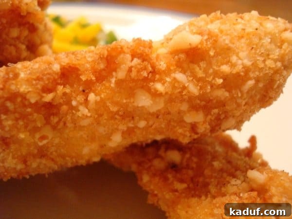 Tropical Macadamia Chicken with Sweet Mango Salsa 3 Two perfectly fried macadamia-crusted chicken strips, golden brown and crunchy, served on a clean white plate.