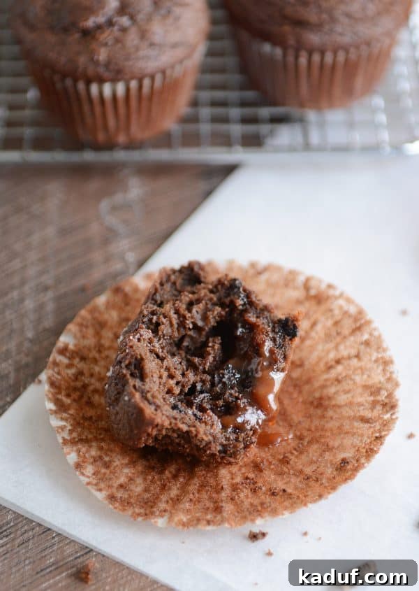 A glorious double chocolate salted caramel muffin, sliced in half, with warm, gooey caramel oozing from its rich chocolate center.