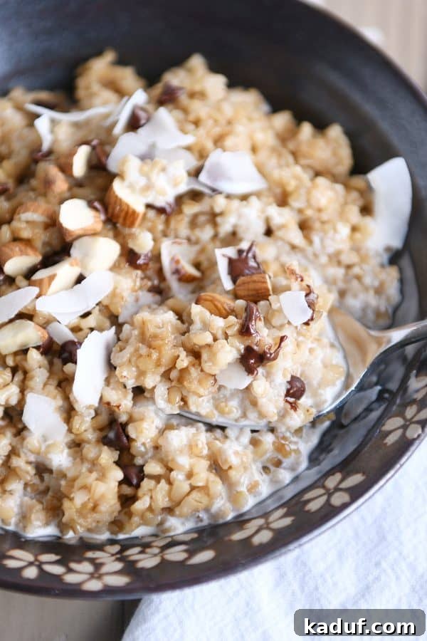 Creamy Coconut Milk Steel Cut Oatmeal in a brown bowl, topped with chocolate chips, almonds, and shredded coconut flakes. A perfect hearty breakfast.