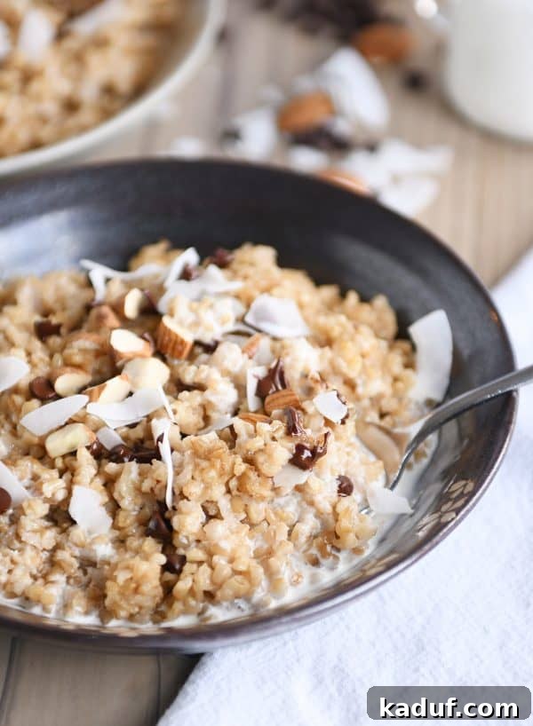 Close-up of creamy Coconut Milk Steel Cut Oatmeal in a brown bowl, with a spoon, garnished with chocolate chips, almonds, and coconut flakes. Emphasizing the rich texture.