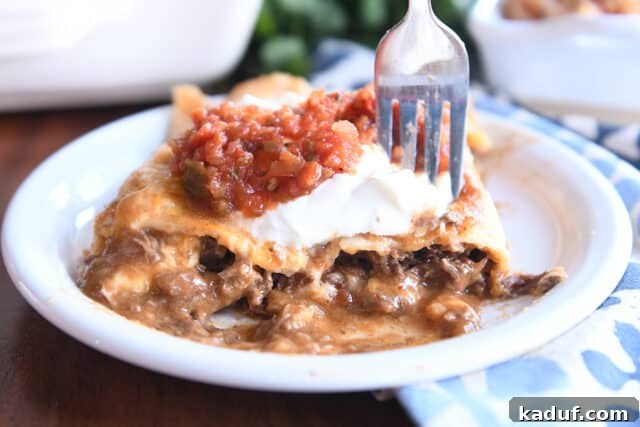 Two saucy enchiladas on white plate with fork.