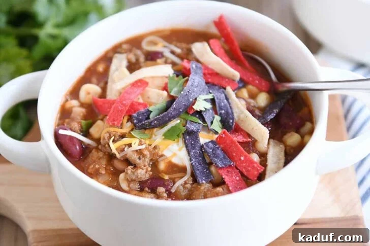 White bowl filled with taco soup, cheese, sour cream and tortilla strips.