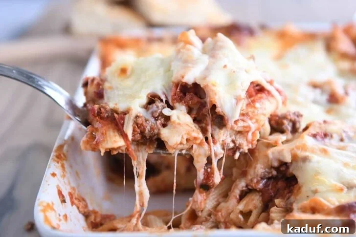 scooping serving of easy cheesy weeknight pasta bake out of white 9X13-inch pan