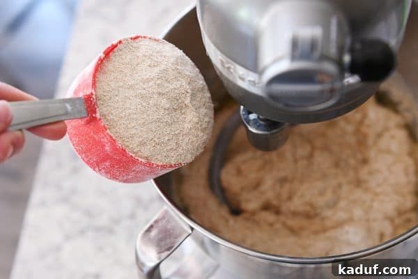 Effortless KitchenAid Small Batch Soft Fluffy Whole Wheat Bread 9 Whole wheat flour being poured into a metal KitchenAid bowl, a crucial step in dough formation.