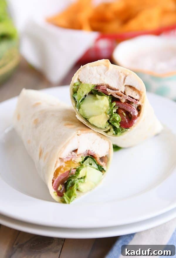 Weeknight Chicken BLT Wraps with Creamy Southwest Zing 2 Chicken BLT burrito cut in half on white plate, revealing layers of chicken, bacon, lettuce, tomato, and avocado.