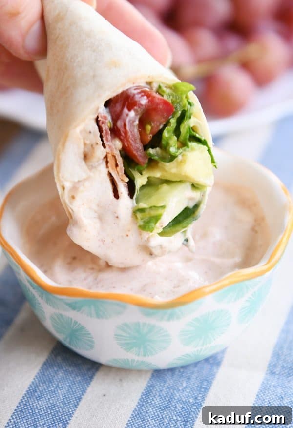 Weeknight Chicken BLT Wraps with Creamy Southwest Zing 3 Close-up of a hand dipping a chicken BLT burrito into a small bowl of creamy Southwest dipping sauce.