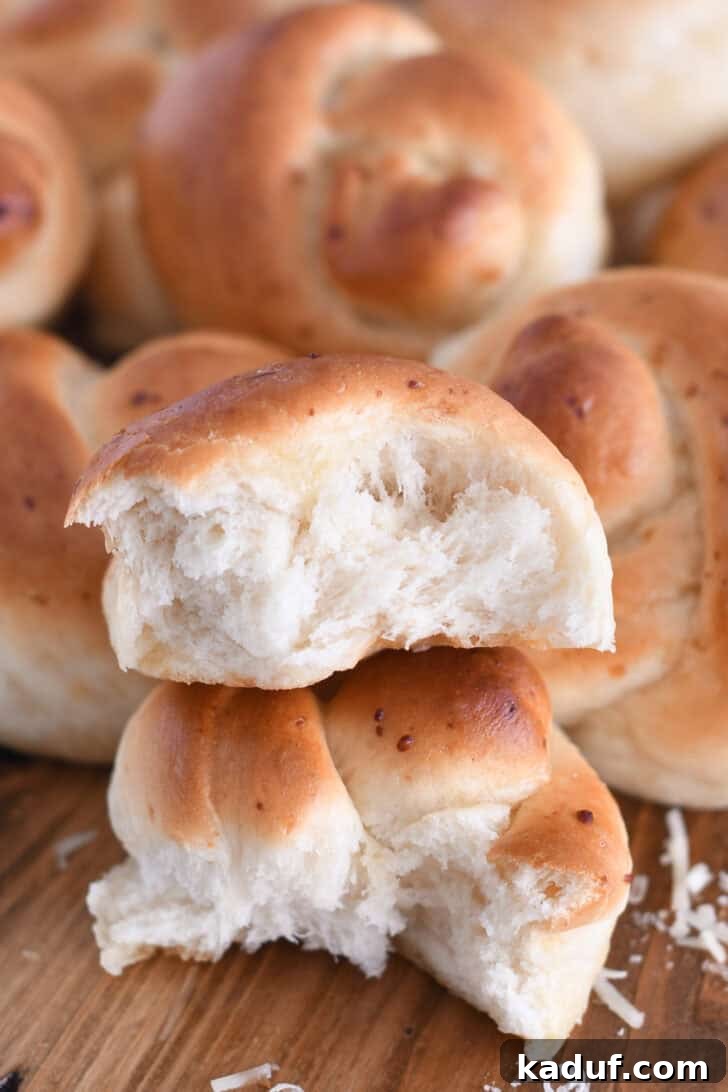 Quick Cheesy Parmesan Knots 12 A Parmesan breadstick knot gently torn open, revealing its soft, fluffy interior and golden crust, with two halves stacked invitingly on a white surface, showcasing its perfect texture.