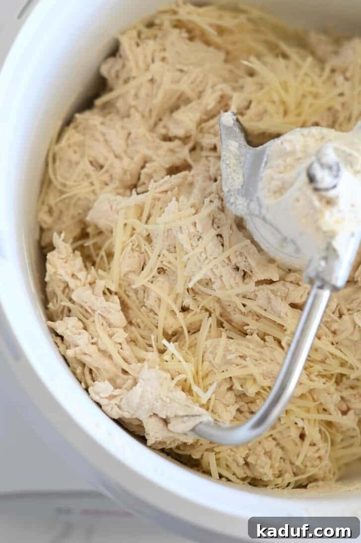 Quick Cheesy Parmesan Knots 3 Freshly grated Parmesan cheese being added to breadstick dough in a white stand mixer with a dough hook attachment, illustrating the flavor infusion step.