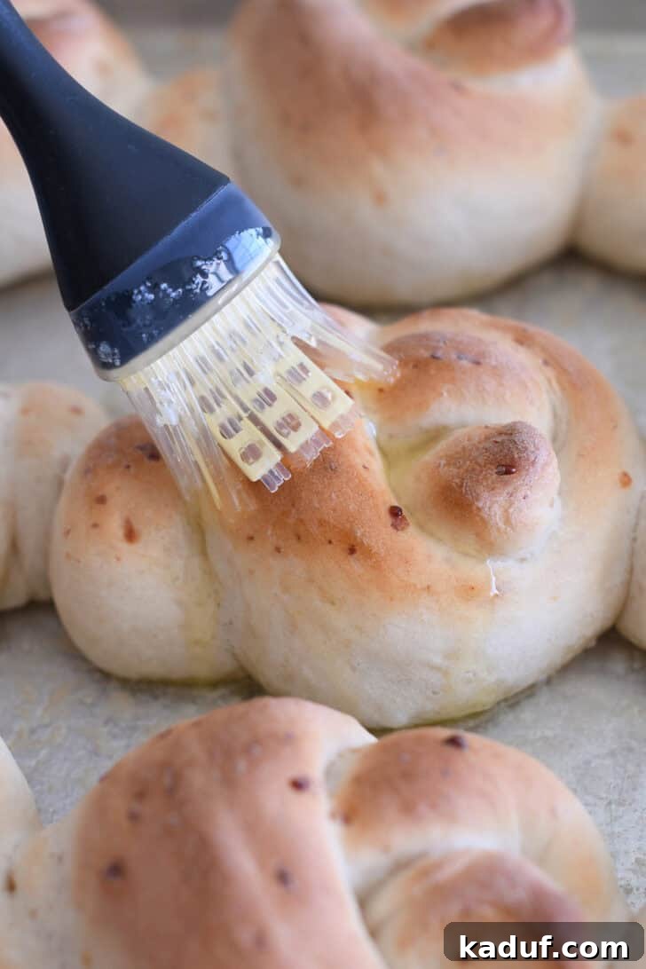 Quick Cheesy Parmesan Knots 6 Melted butter being generously brushed over the top of a hot, freshly baked Parmesan breadstick knot, creating a glistening, golden finish and enhancing its rich flavor.