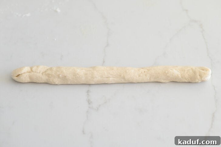 Quick Cheesy Parmesan Knots 7 A portion of breadstick dough rolled into a long, thin strip on a clean white countertop, perfectly prepared and ready for the knot formation process.