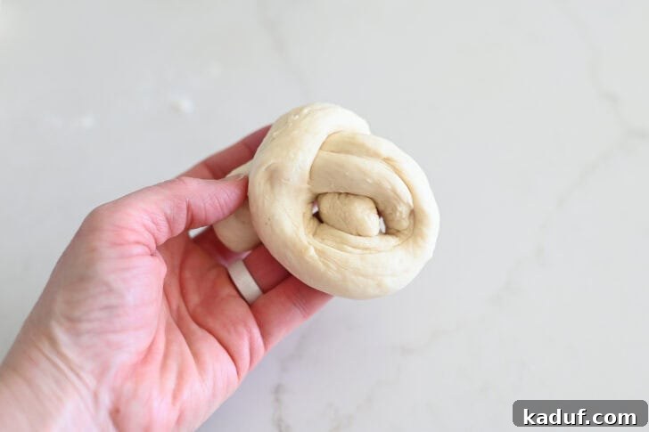 Quick Cheesy Parmesan Knots 9 Hands guiding the end of the breadstick dough through the loop, illustrating the crucial step to complete the formation of a perfect dough knot.