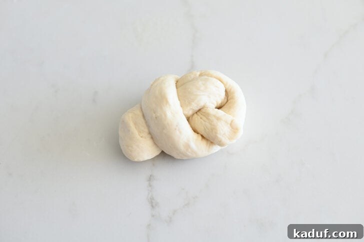 Quick Cheesy Parmesan Knots 10 A freshly shaped breadstick dough knot resting on a white countertop, showcasing its simple yet elegant form, ready for proofing.