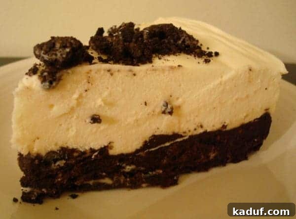 Oreo Crunch White Chocolate Mousse Torte 2 A slice of elegant white chocolate mousse torte with a dark Oreo crust, served on a white plate, highlighting its creamy texture.