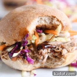 A delicious honey balsamic BBQ pork sandwich with a bite taken out, served on a white plate, ready to be devoured.
