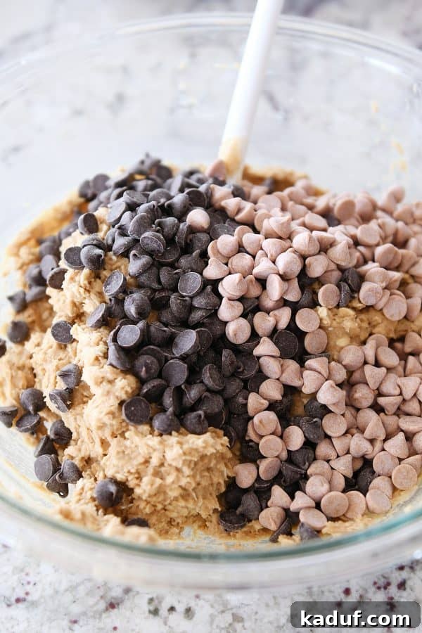 Bowl of monster cookie dough with chocolate chips and butterscotch chips about to be mixed in, showcasing the rich texture.