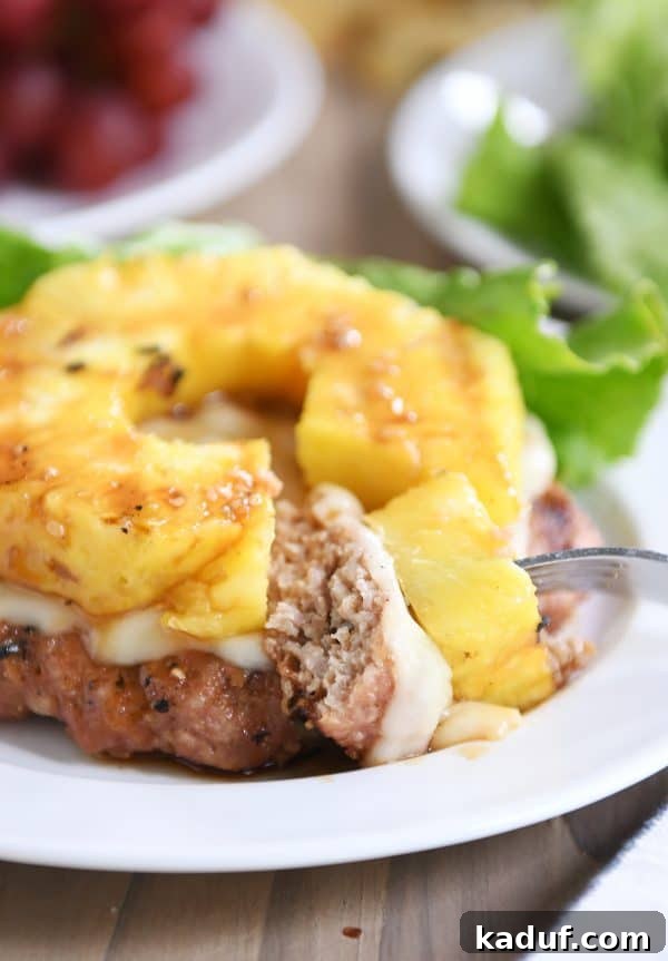 Tropical Teriyaki Turkey Burgers with Grilled Pineapple 7 A Teriyaki Turkey Burger with grilled pineapple and melted Swiss cheese, with a delicious bite taken, showing its juicy interior.