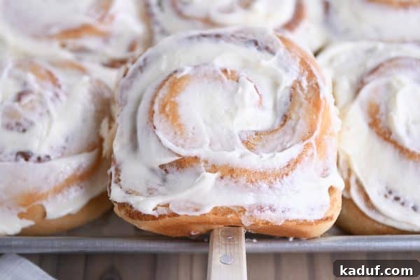 Friday Focus: Mastering the Summer Months 15 A spatula lifting a frosted cinnamon roll from a baking pan, a comforting and popular signature recipe.