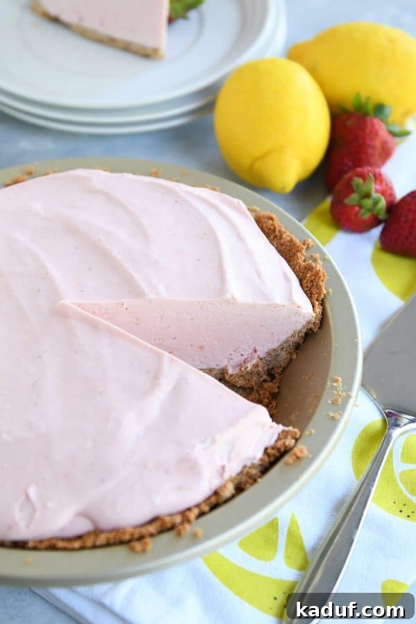 Pink Lemonade Strawberry Bliss Pie 3 A vibrant frozen strawberry lemonade pie with a slice carefully removed, revealing its creamy texture.