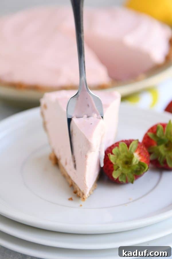 Pink Lemonade Strawberry Bliss Pie 4 A fork digging into a bite of creamy frozen strawberry lemonade pie, highlighting its smooth texture and golden crust.