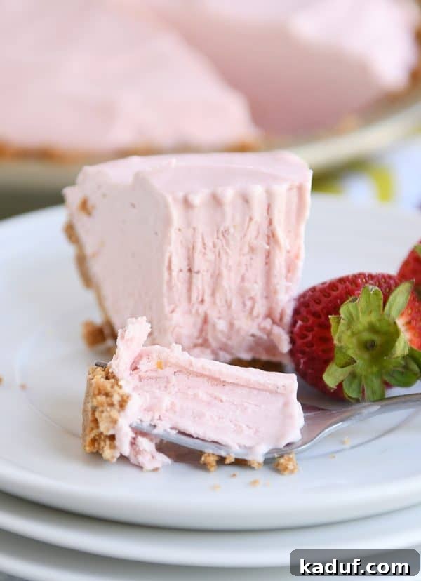 Pink Lemonade Strawberry Bliss Pie 5 A slice of frozen strawberry lemonade pie with a bite taken out, served on a pristine white plate.