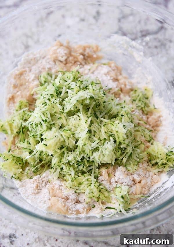 Moist Zucchini Banana Bliss 4 Glass bowl filled with zucchini banana bread batter, with freshly shredded zucchini piled on top, ready to be folded in.
